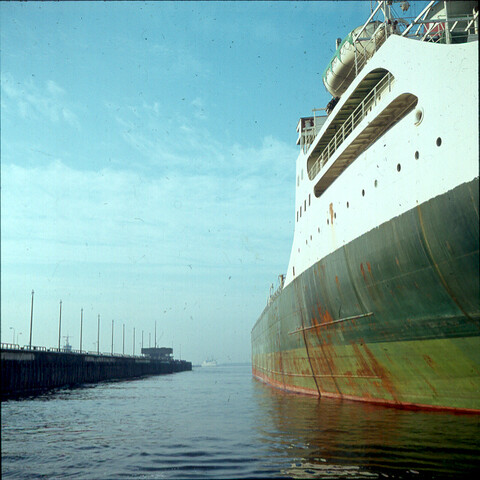 S.9100(1150); Dia van de Noordersluis in IJmuiden, doorkijkje langs wand van grote tanker [...]; diapositief