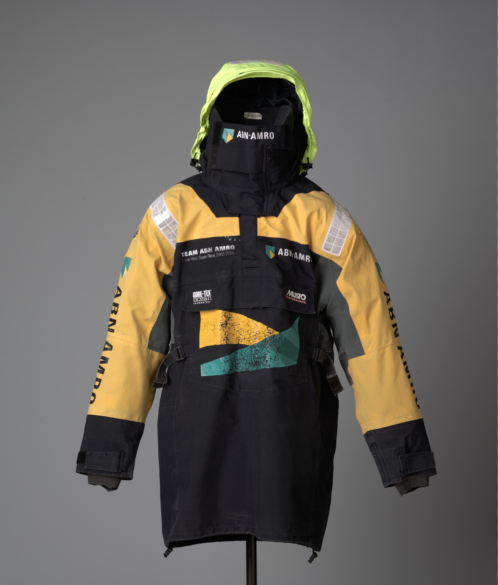 2007.0201; Zwart zeiljack met gele schouderstukken, gele en grijze mouwen van het merk Musto. Bedrukt met het logo van ABN AMRO; kleding