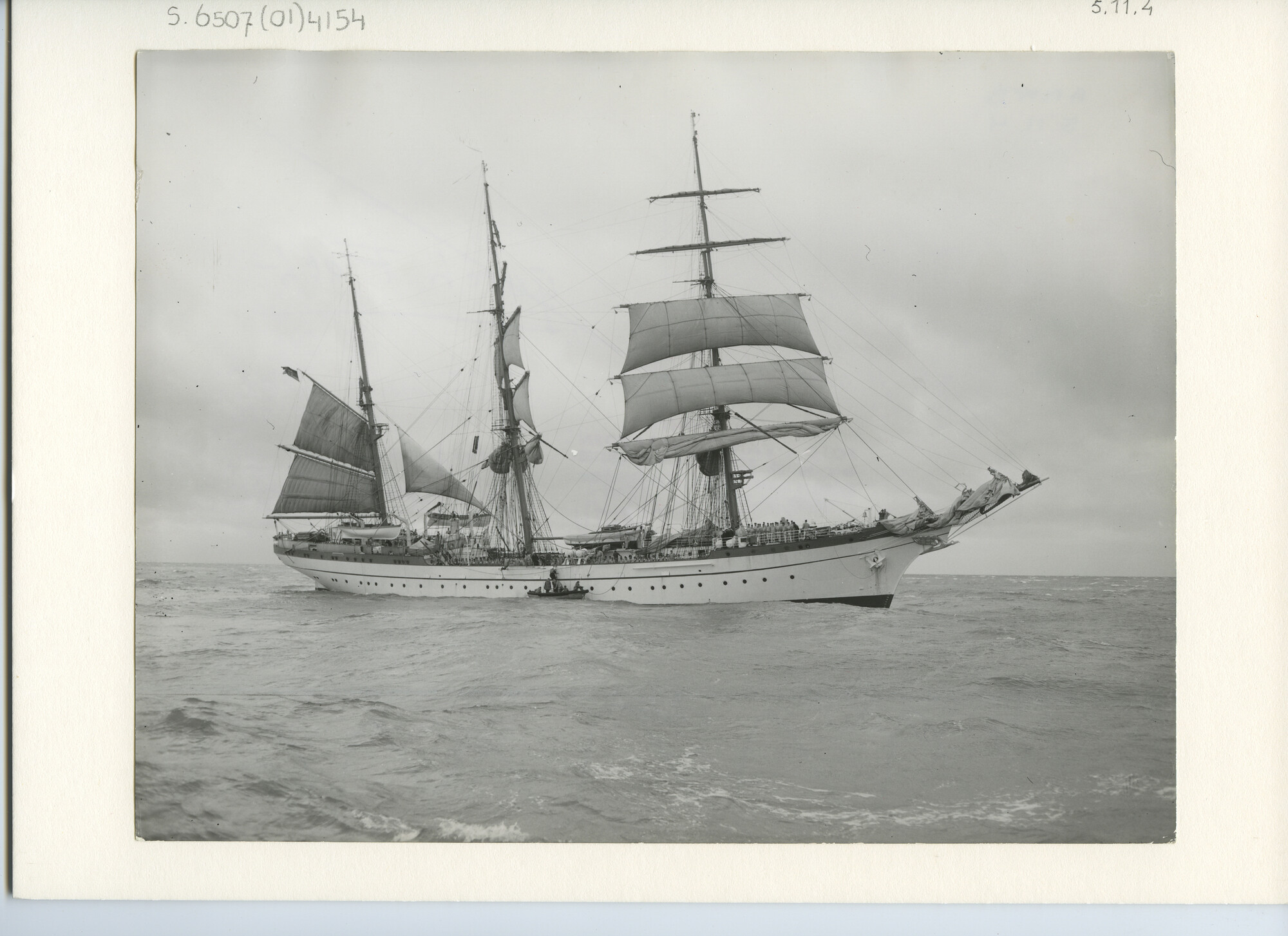 S.6507(01)4154; Foto van het Duitse schoolschip, de witte stalen bark Gorch Fock II (1958) bijgedraaid op zee met een sloep langszij; foto