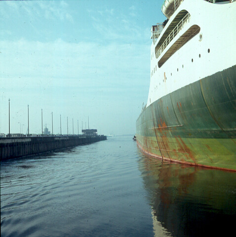 S.9100(1149); Dia van de Noordersluis in IJmuiden, doorkijkje langs wand van grote tanker [...]; diapositief
