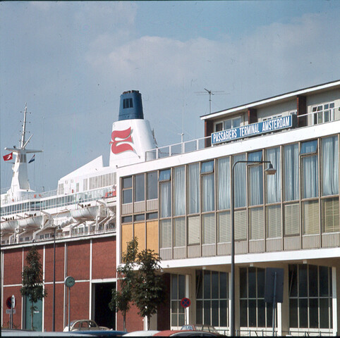 S.9100(6932); Dia voorzijde gebouw PTA met daarachter het Noorse cruiseschip 'Royal Viking Sea' van de Royal Viking Line; diapositief