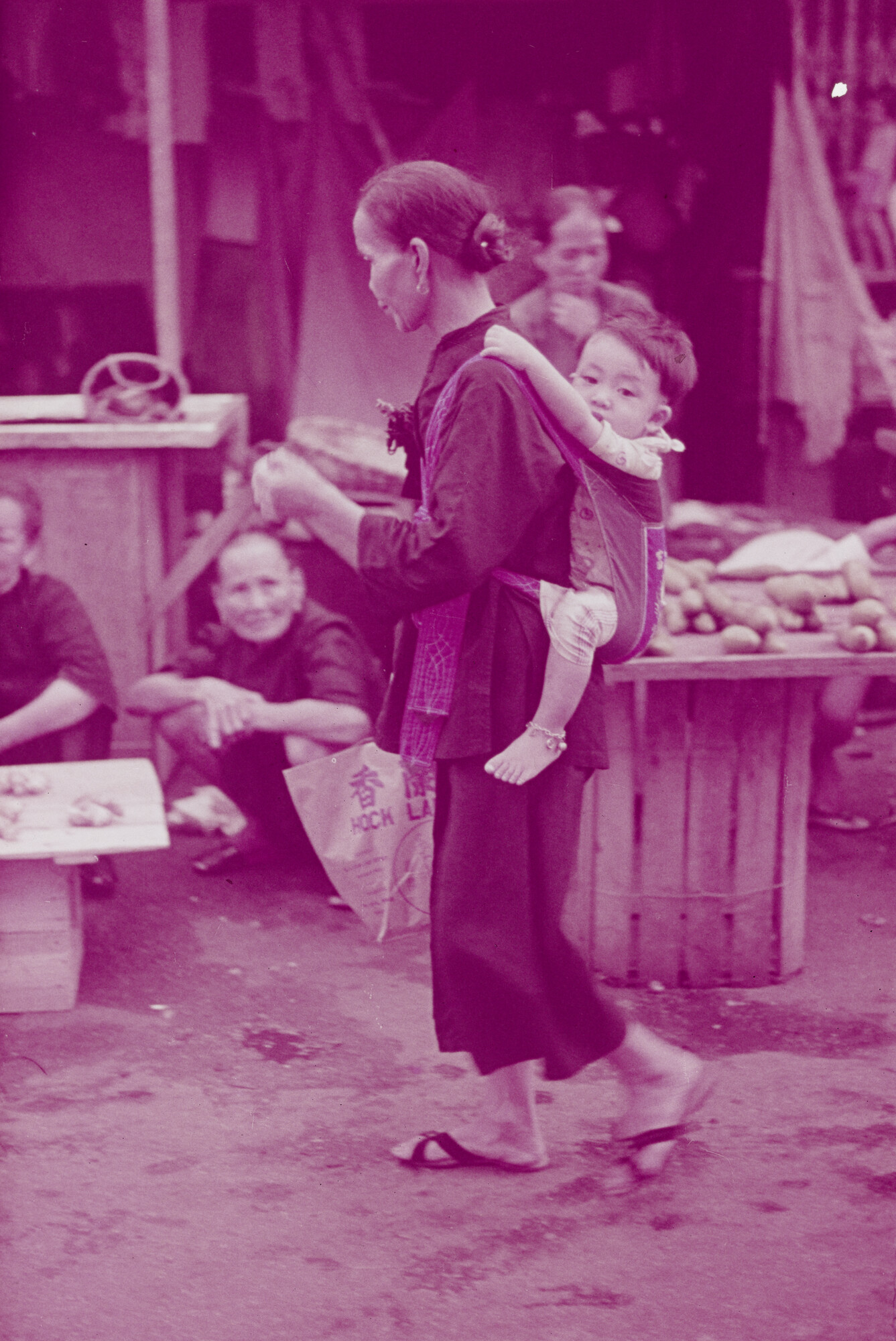 2015.0455; Dia van een vrouw met een kind op haar rug in een straat met marktkramen in Singapore; diapositief