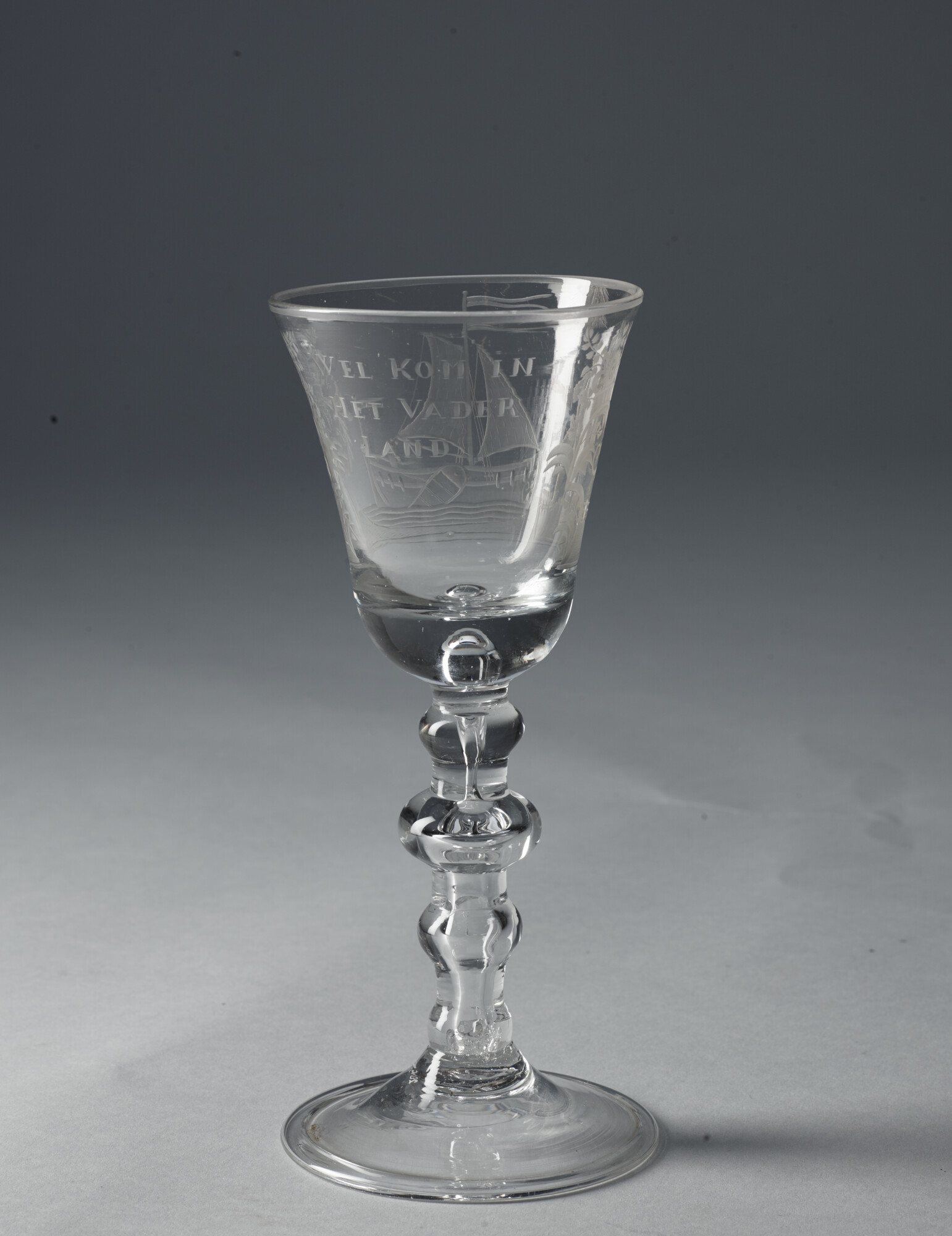 2019.0579; Vriendschapsglas met een radgravure van een staande man met een glas in zijn hand die wacht op een beurtscheepje. Met de inscriptie “Welkom in het Vaderland”; gelegenheidsglas