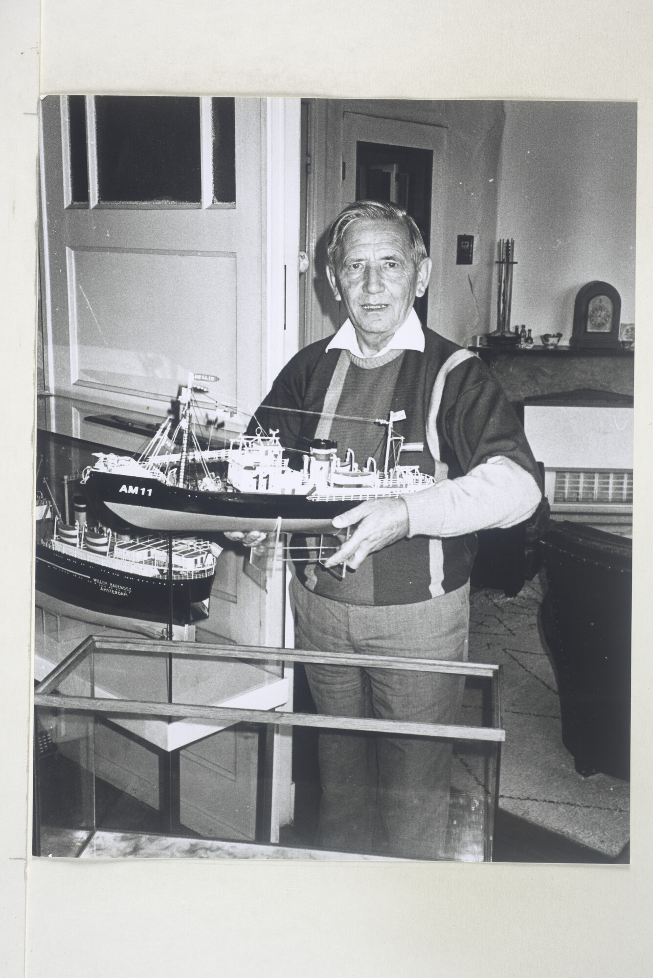 1999.3037; Jaap Roda poseert in zijn huiskamer met een scheepsmodel van de walvisjager "Nellie W. Vinke" (AM 11) naast het model van de "Willem Barendsz"; foto