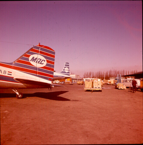 S.9100(2215); Dia (sfeerbeeld) Schiphol: Achterstuk MAC vliegtuig en KLM vliegtuig; diapositief