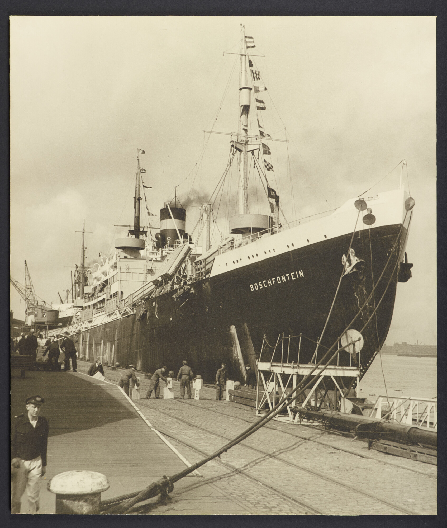 S.5232(28)04; Zwart-wit foto van het tot troepentransportschip verbouwde vrachtpassagiersschip ms. Boschfontein aan de kade, Amsterdam; foto