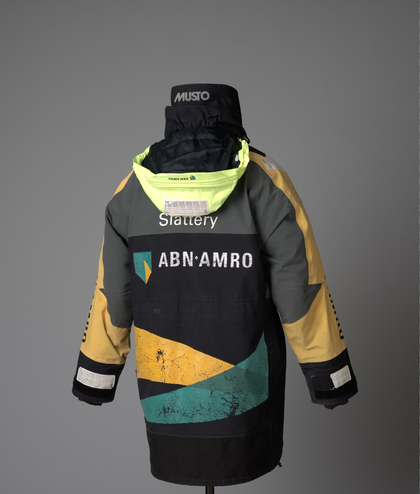 2007.0201; Zwart zeiljack met gele schouderstukken, gele en grijze mouwen van het merk Musto. Bedrukt met het logo van ABN AMRO; kleding