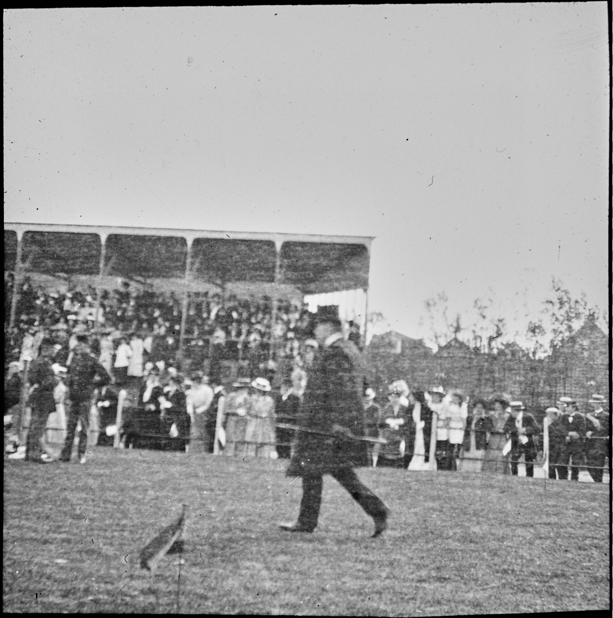 S.1156(06)375-07; Lantaarnplaatje van de heer Scholten lopend op een veld met publiek op een tribune; lantaarnplaatje