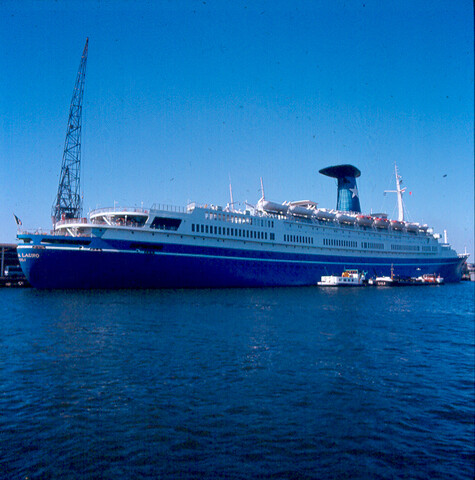 S.9100(7016); Dia van het Italiaanse cruiseschip Angelino Lauro (ex- Oranje van de SMN) afgemeerd bij de PTA in Amsterdam vanaf het water [...]; diapositief